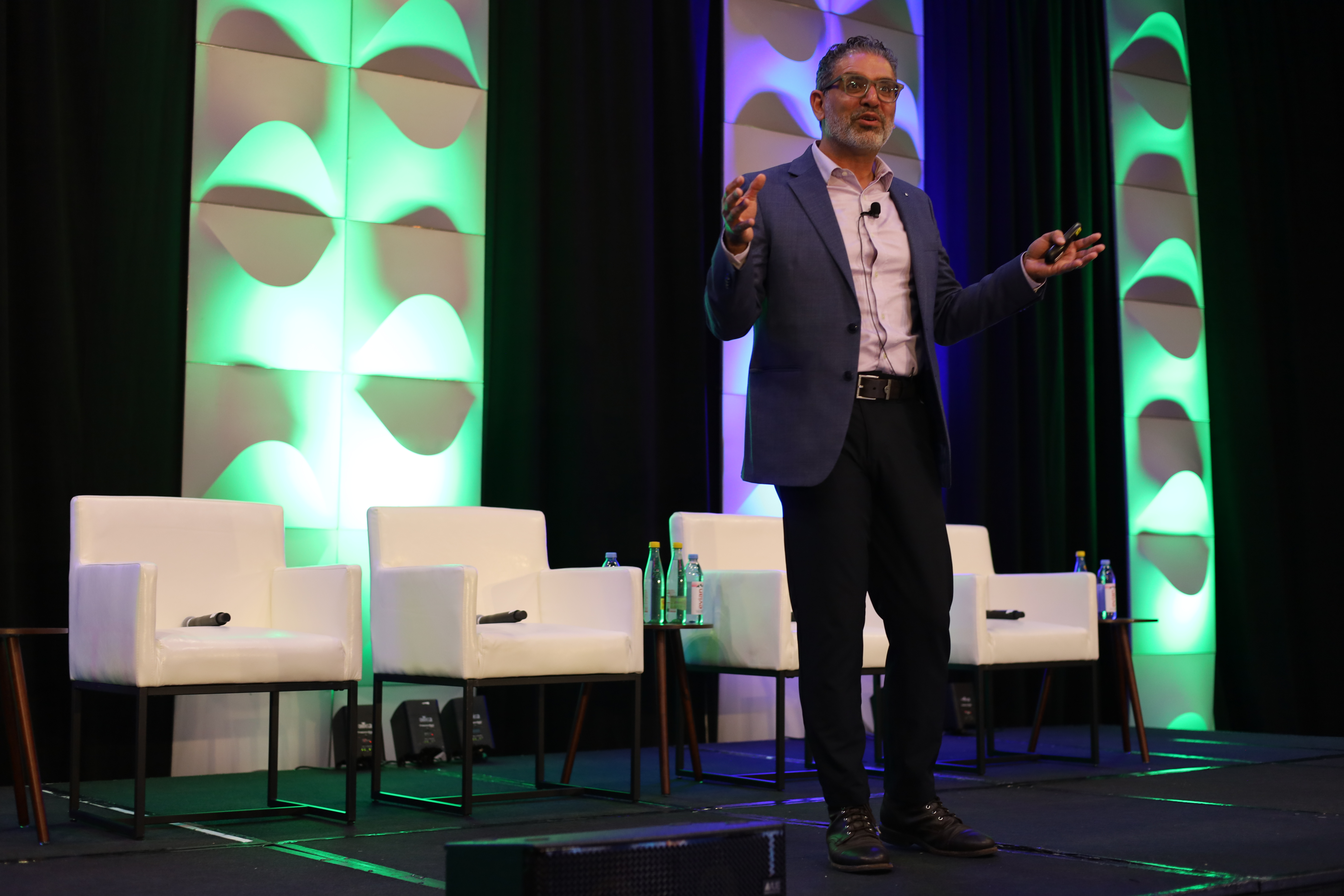 Moudy Elbayadi speaking on stage with green and blue lighting